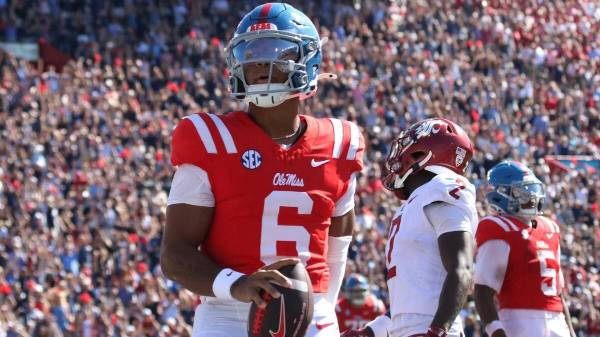 Ole Miss quarterback holds a football as Louisville and Ole Miss players stand nearby during a game.