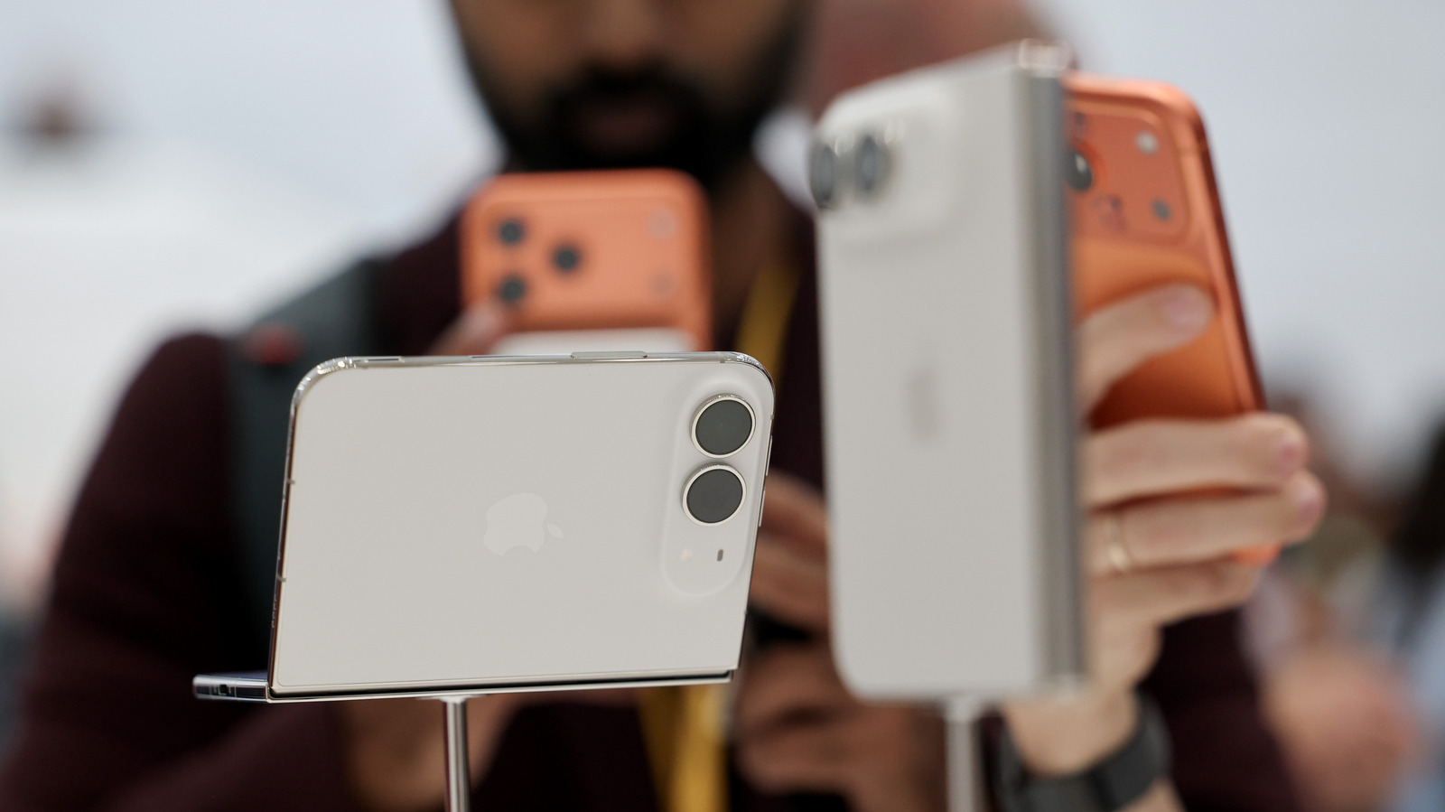 Several people hold smartphones, including white and orange foldable phones, in a close-up display.