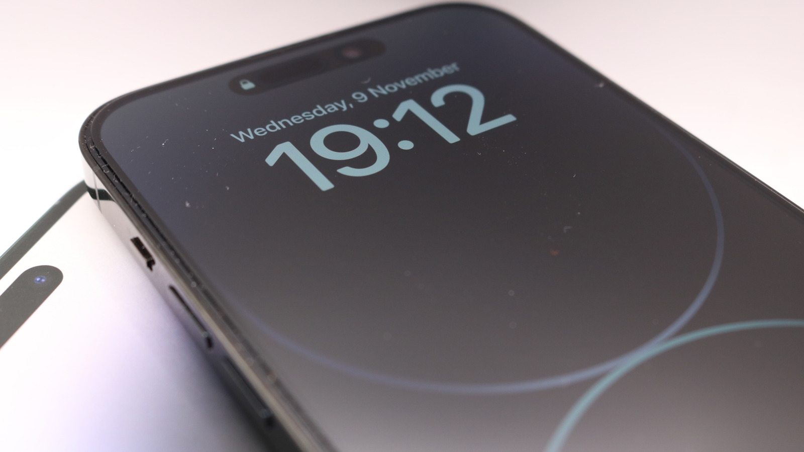 Close-up of a black iPhone showing its Always-On Display with the time 19:12 and date Wednesday, 9 November.