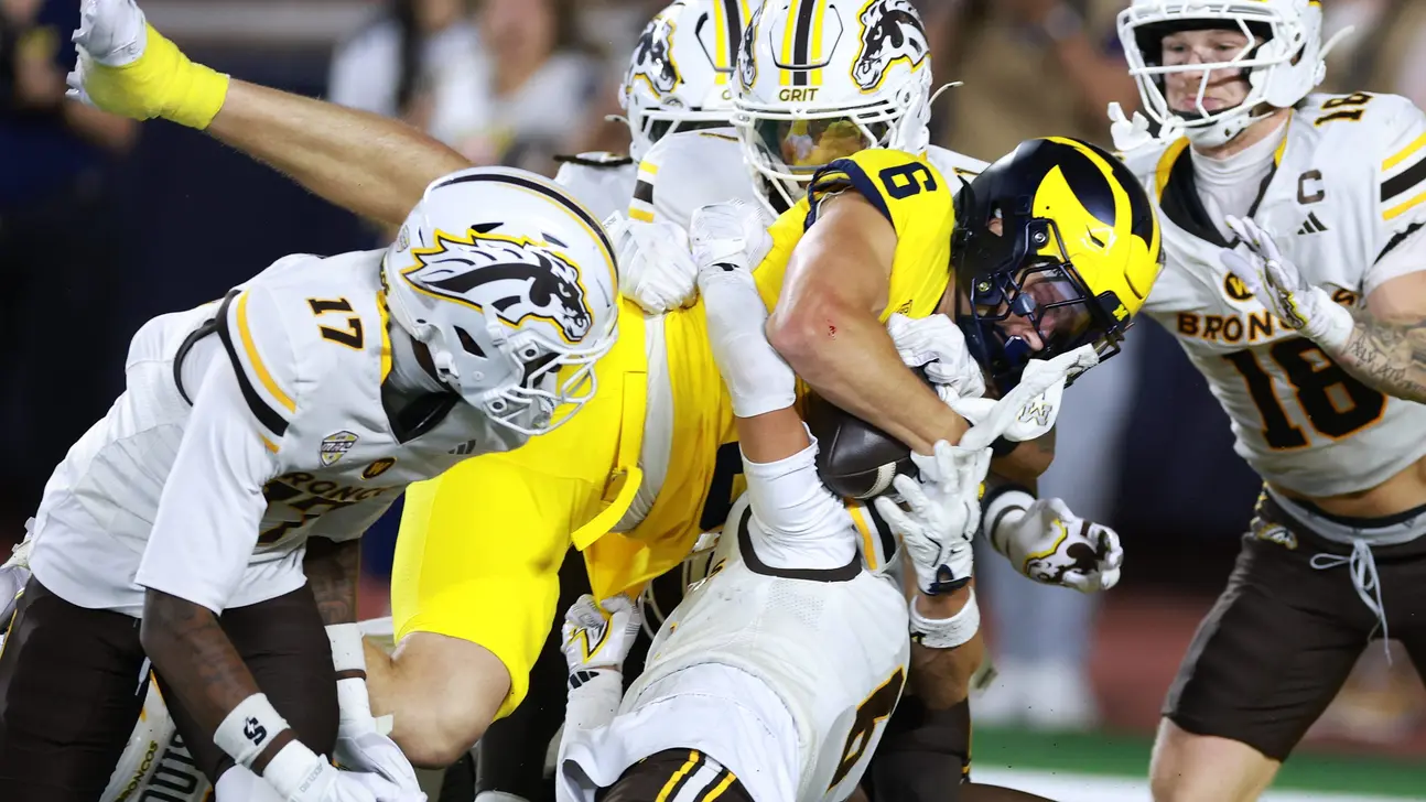 Football players in white and maize uniforms collide during a contested play.