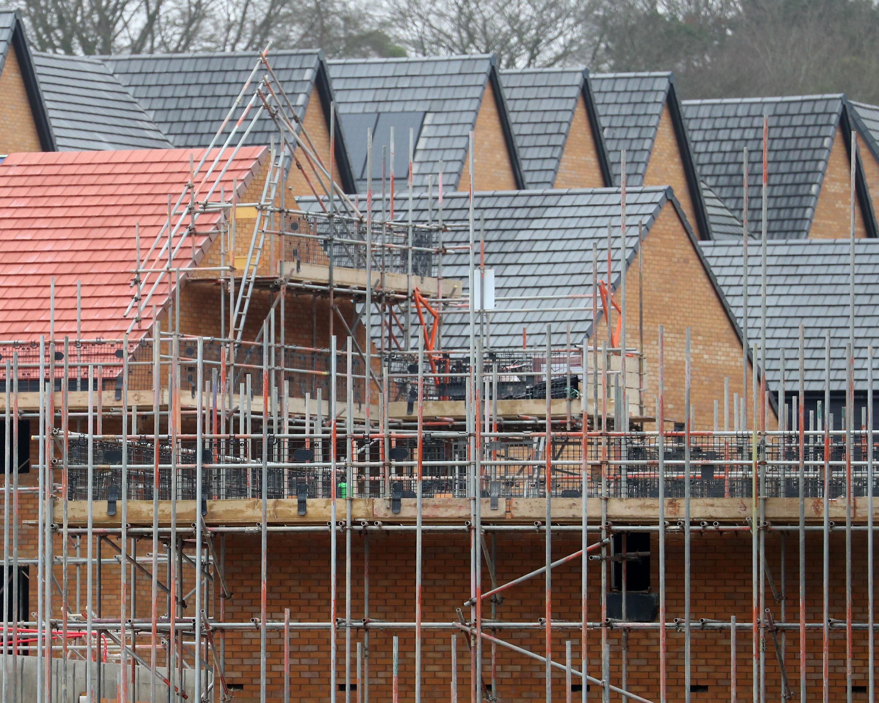 Partially built brick houses surrounded by extensive metal scaffolding and tiled roofs.