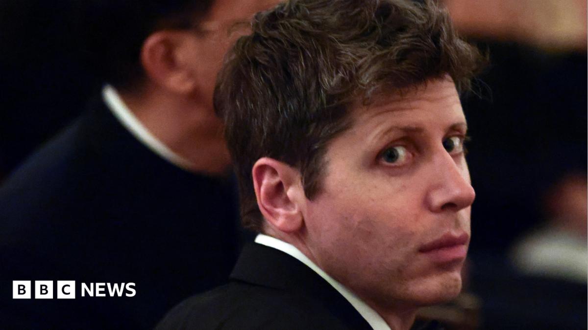 A man in a dark suit looks over his shoulder at an indoor event, with BBC News branding.