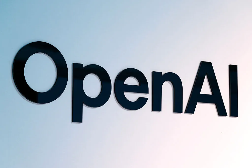 Black OpenAI logo lettering mounted on a pale blue and white wall