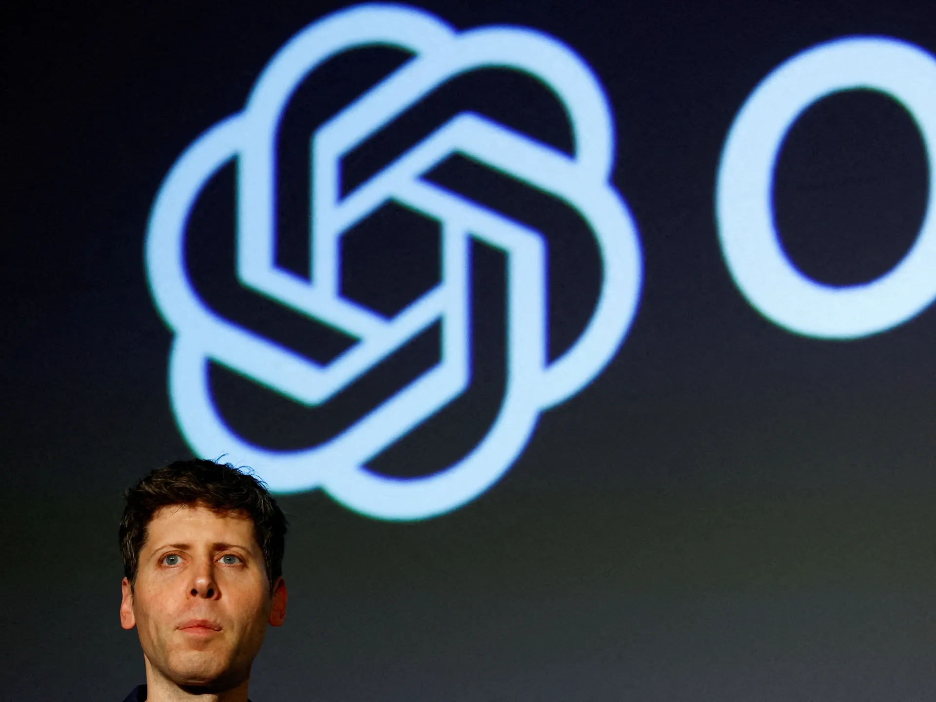 OpenAI logo projected on a dark screen above a partially visible man