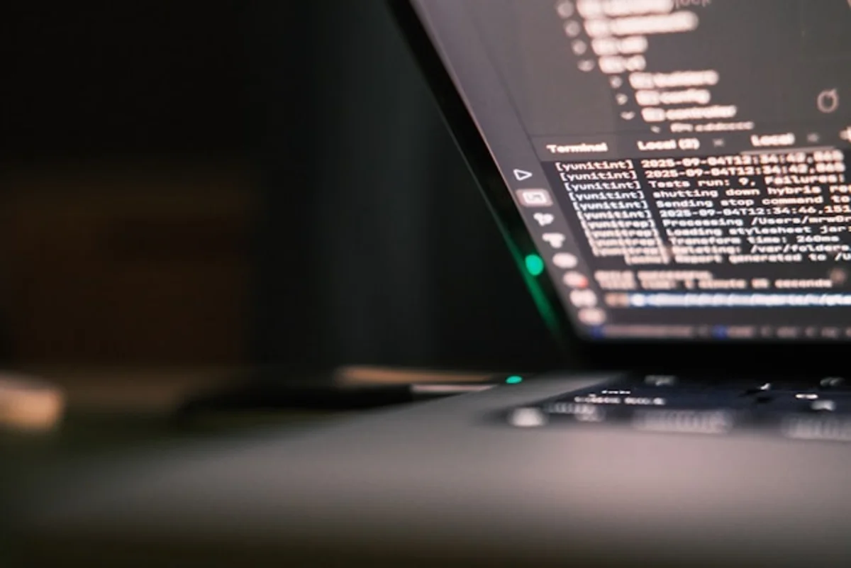 Blurred laptop screen displaying terminal code beside a dark keyboard and glowing indicator light.