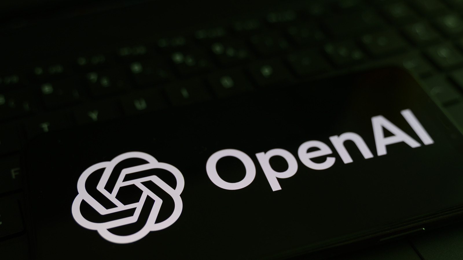 OpenAI logo and wordmark displayed on a dark laptop screen beside a keyboard.