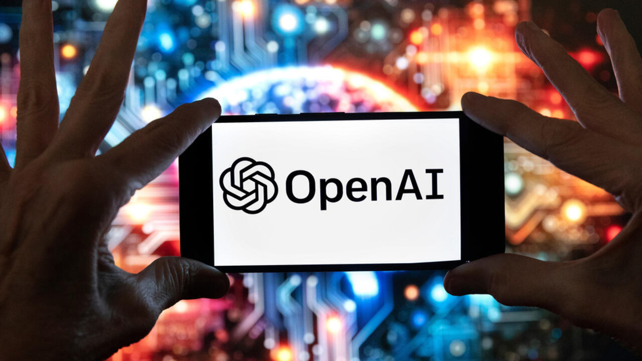 Hands hold a smartphone displaying the OpenAI logo against a colorful, abstract technology background.