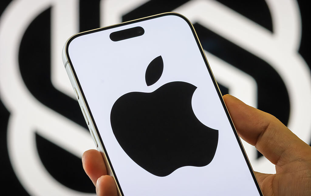 Hand holding an iPhone displaying a large black Apple logo against a contrasting backdrop
