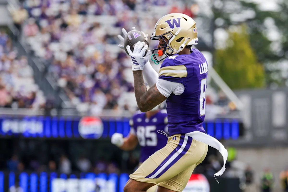 Washington football player in purple and gold catches a football during a game.