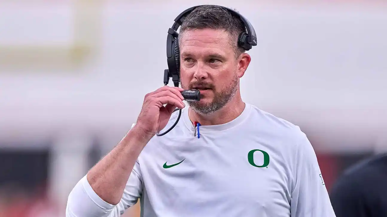 Man in an Oregon shirt wearing a headset and speaking into its microphone.