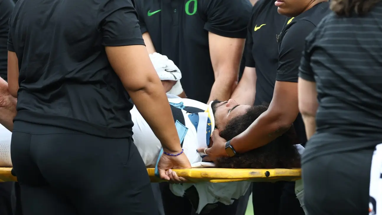 Medical staff carry a football player on a stretcher while supporting his head and neck.