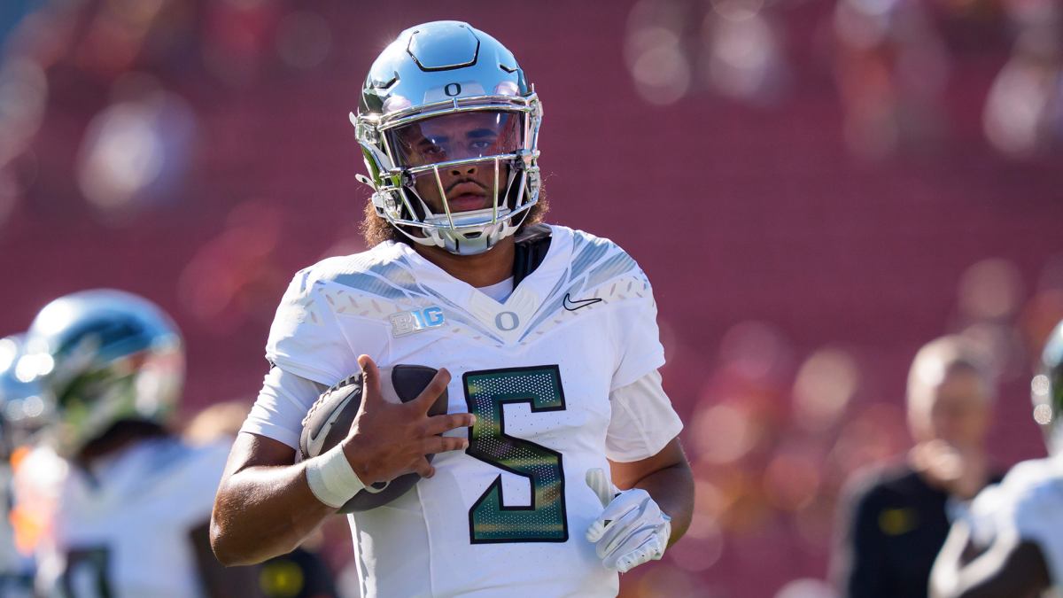 Oregon quarterback in a white number 5 uniform holds a football during a game.