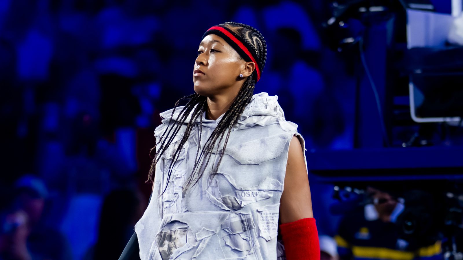 Athlete wearing a distressed white sleeveless outfit, red headband and red arm sleeve under blue lighting