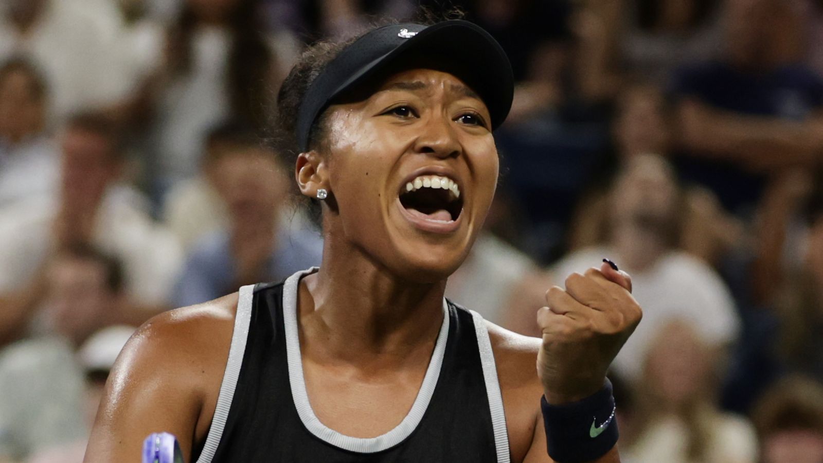 Tennis player in black visor celebrates with clenched fist and open-mouthed smile amid crowd