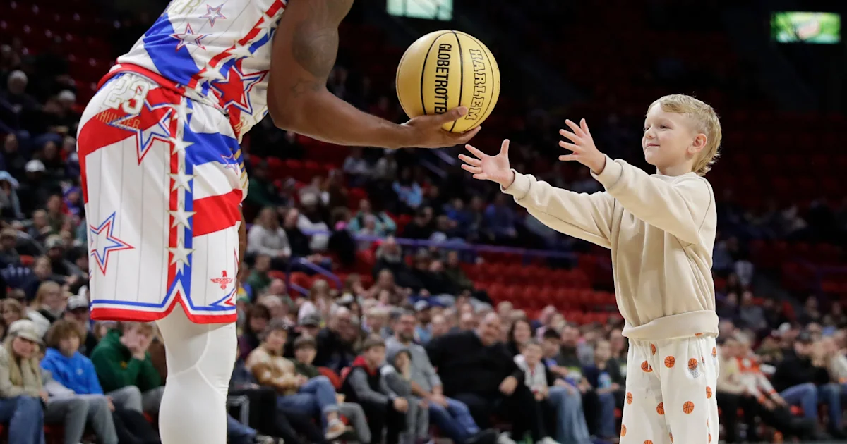 A young child reaches for a basketball held by a cropped performer in a star-patterned uniform.