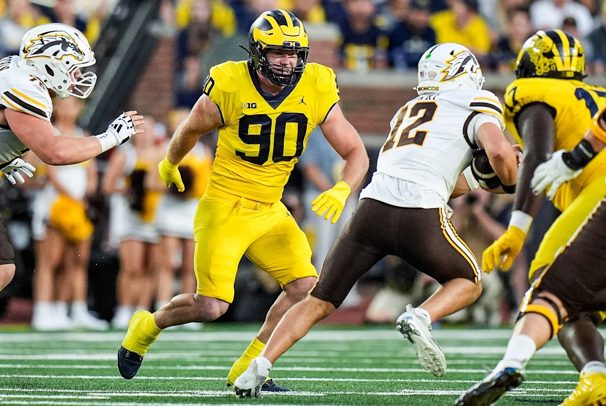 Michigan football player wearing number 90 runs between opposing players during a game