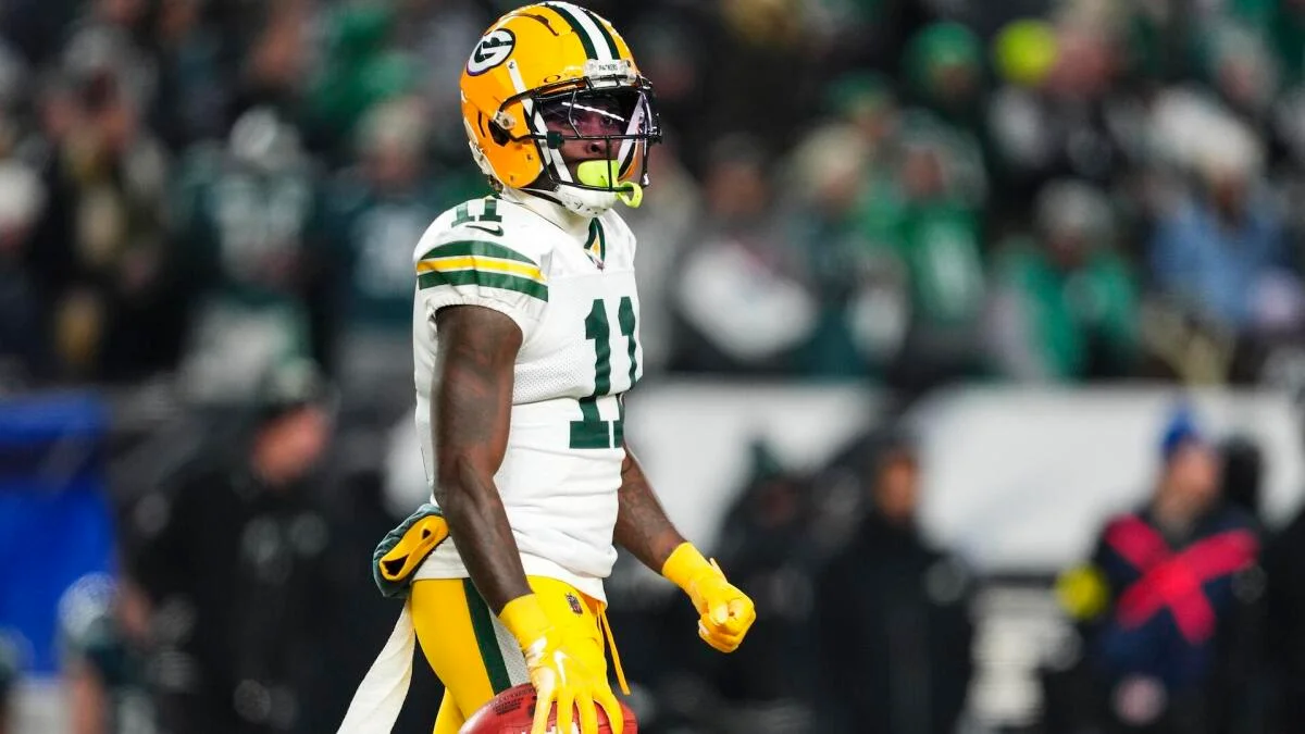 Green Bay Packers player in uniform stands on a football field holding a football.