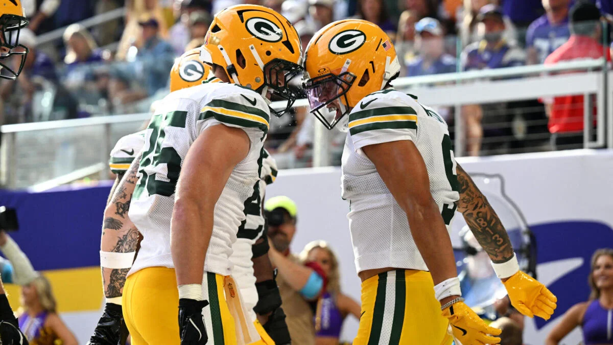 Green Bay Packers players in helmets and white uniforms confer during an NFL game.