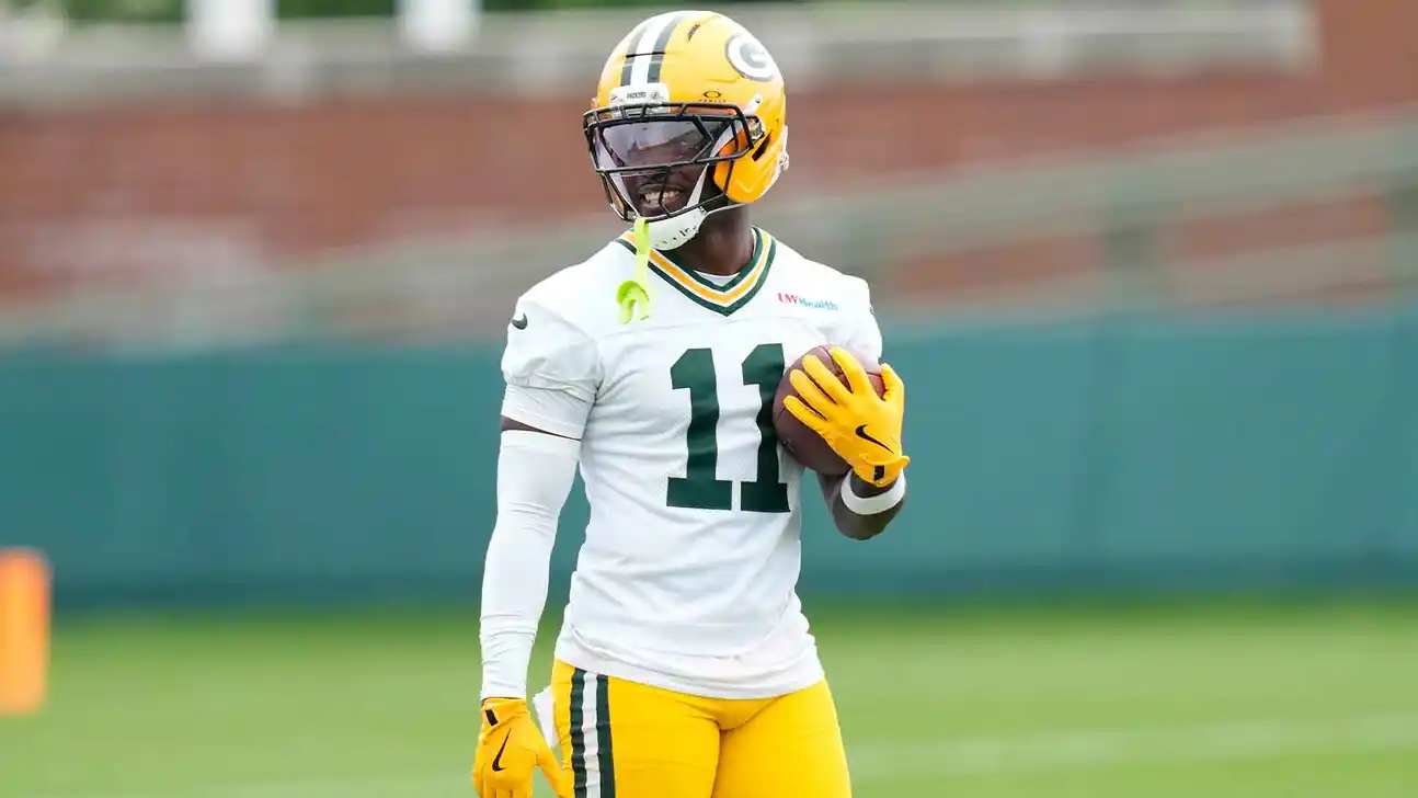 Football player in a yellow helmet and white number 11 jersey holds a football during practice.