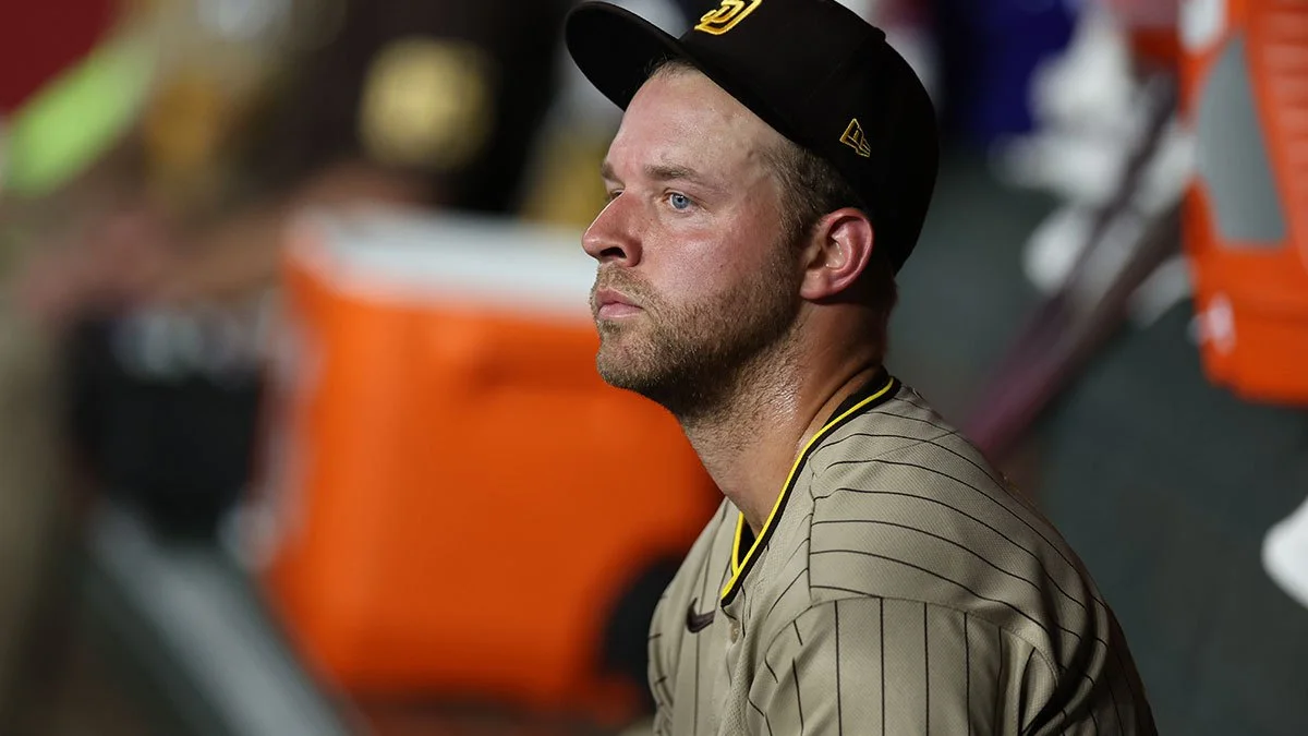 A bearded man in a black cap and gray pinstriped jersey looks to the left against a blurred background.