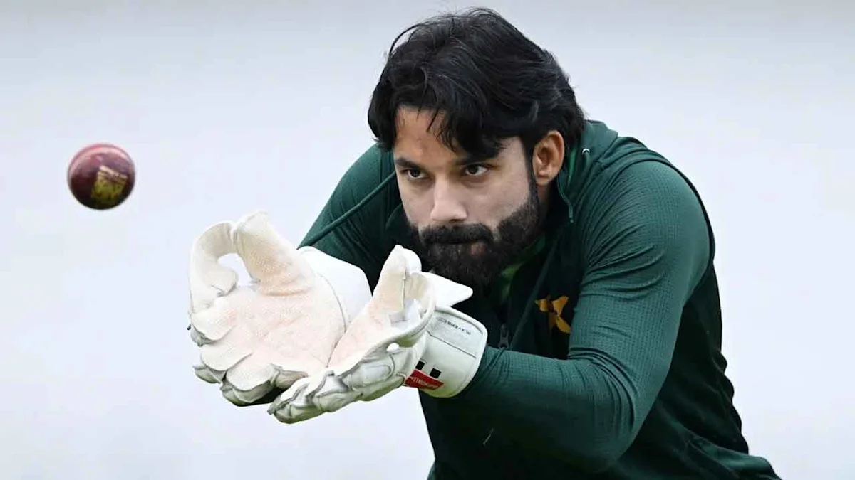 Cricketer in green uniform reaching forward with wicketkeeping gloves as a ball approaches.