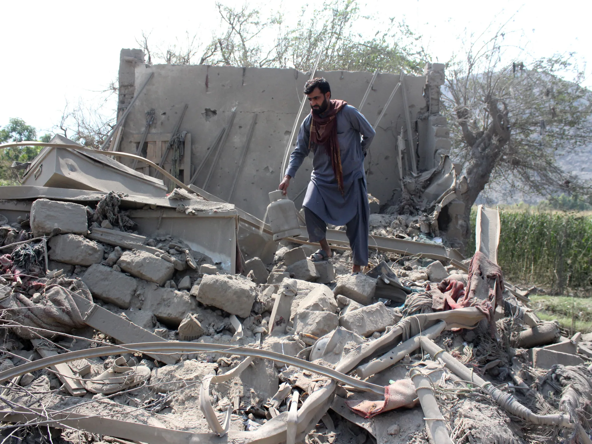 A man in blue clothing stands amid rubble beside a severely damaged concrete building.