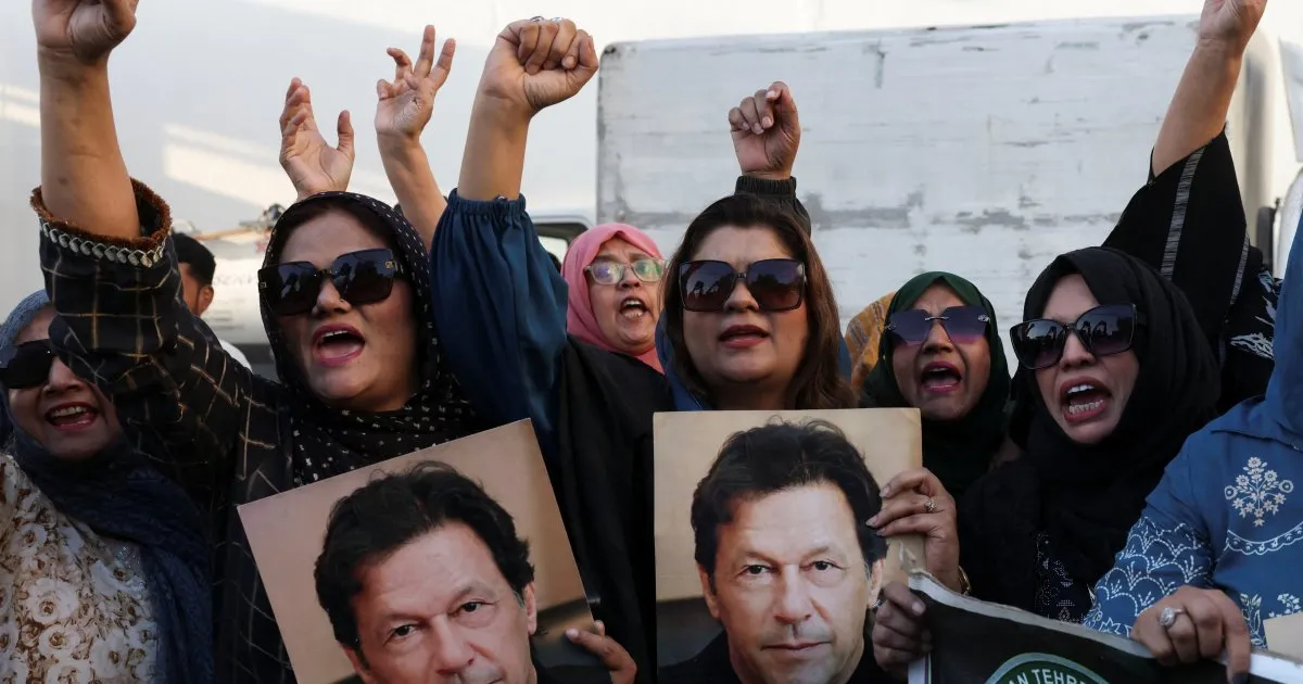A crowd of women in headscarves and sunglasses raise their hands and hold portraits of Imran Khan.