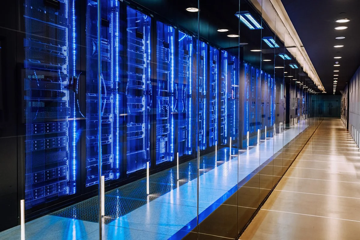 Blue-lit server racks line a glass-walled data center corridor.