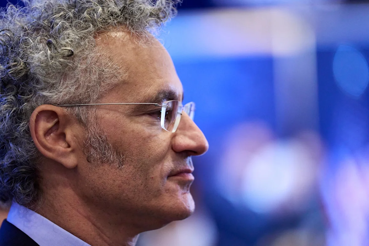 Gray-haired man wearing glasses shown in profile against a blue, softly blurred background