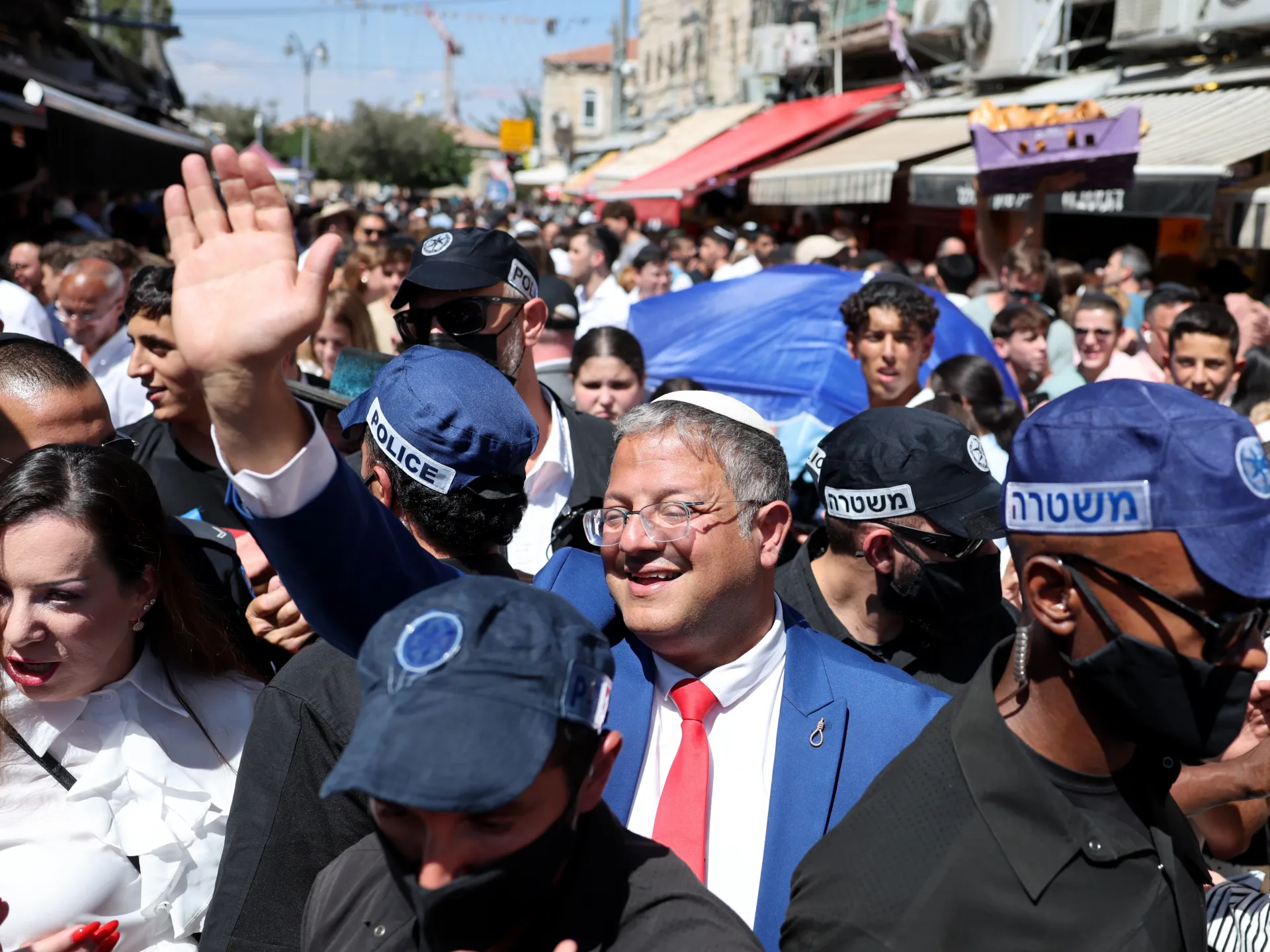Police surround a suited man amid a dense crowd on a busy market street
