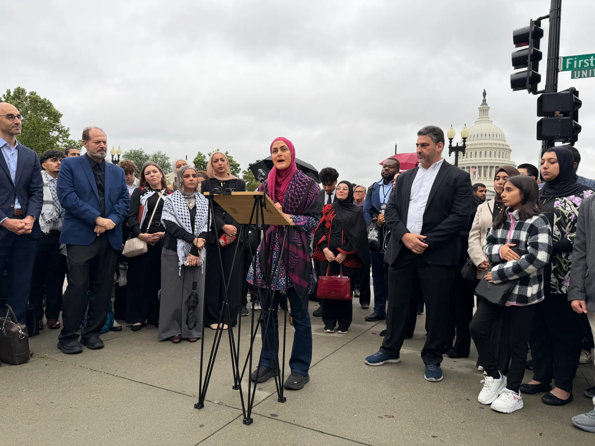 Woman speaks at a podium as a diverse crowd gathers near the U.S. Capitol.