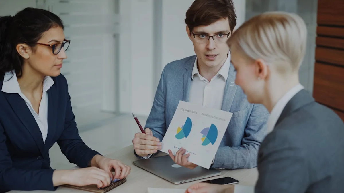 Three business professionals discuss charts during a meeting around a conference table.