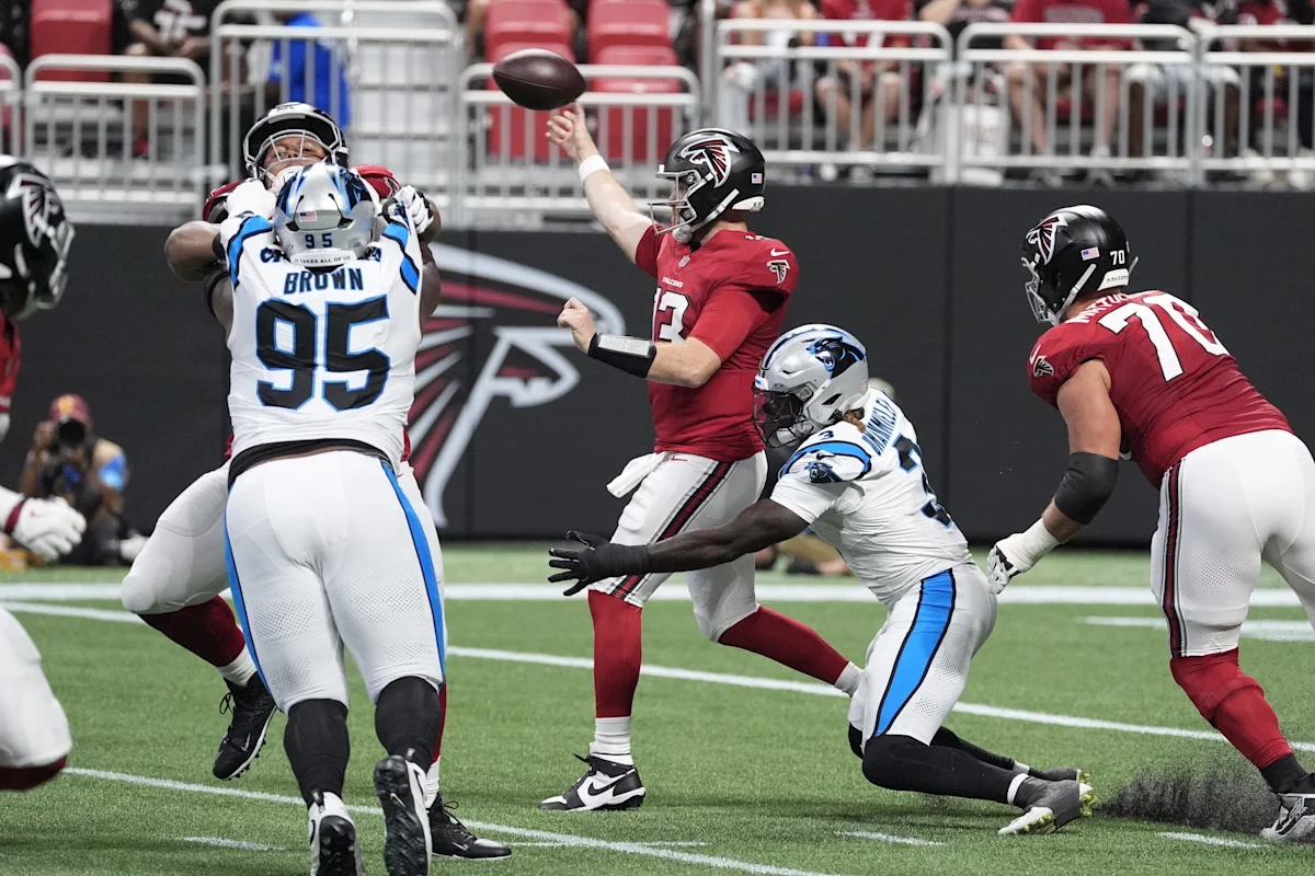 Atlanta quarterback throws a football as Panthers defenders pressure him during a game.