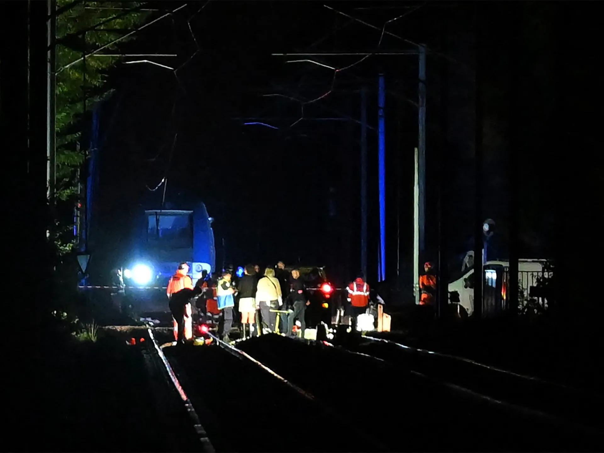 Emergency responders gather beside derailed passenger train cars on a dark railway track at night.