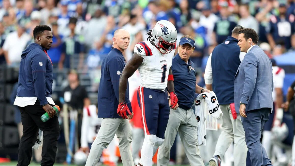 Patriots player in uniform is escorted off the field by team staff