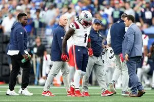 Football player in Patriots uniform walks off field with staff members during a game.