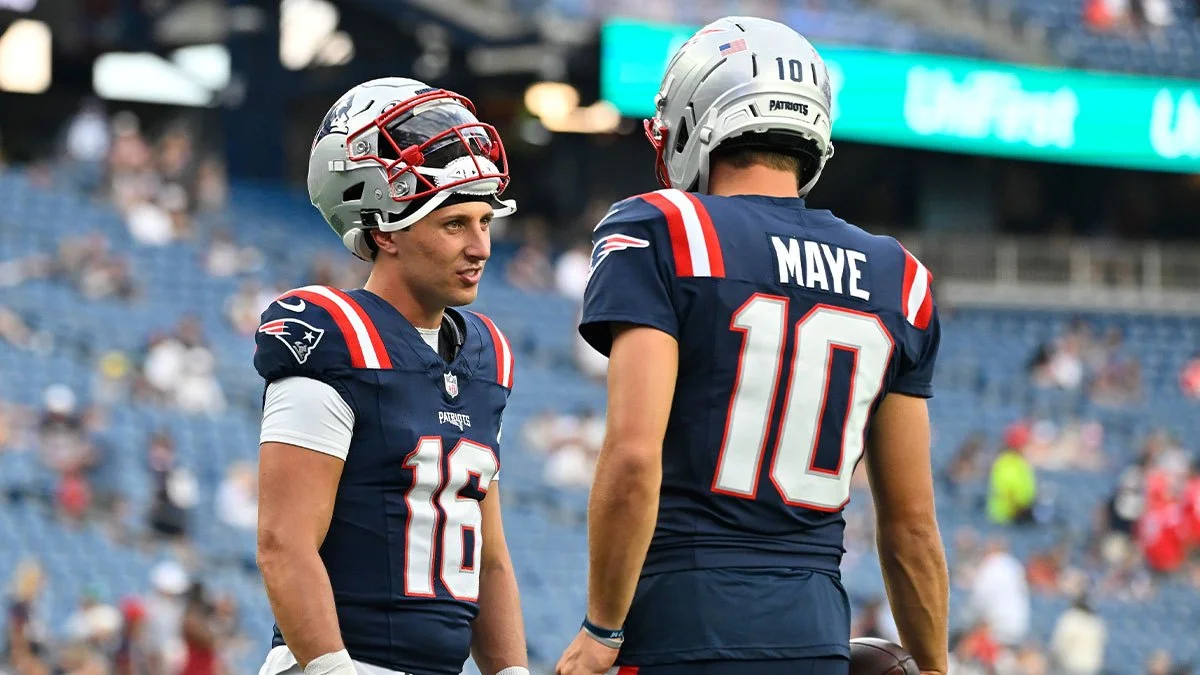 Two New England Patriots players in navy uniforms stand together on the field, one facing away.