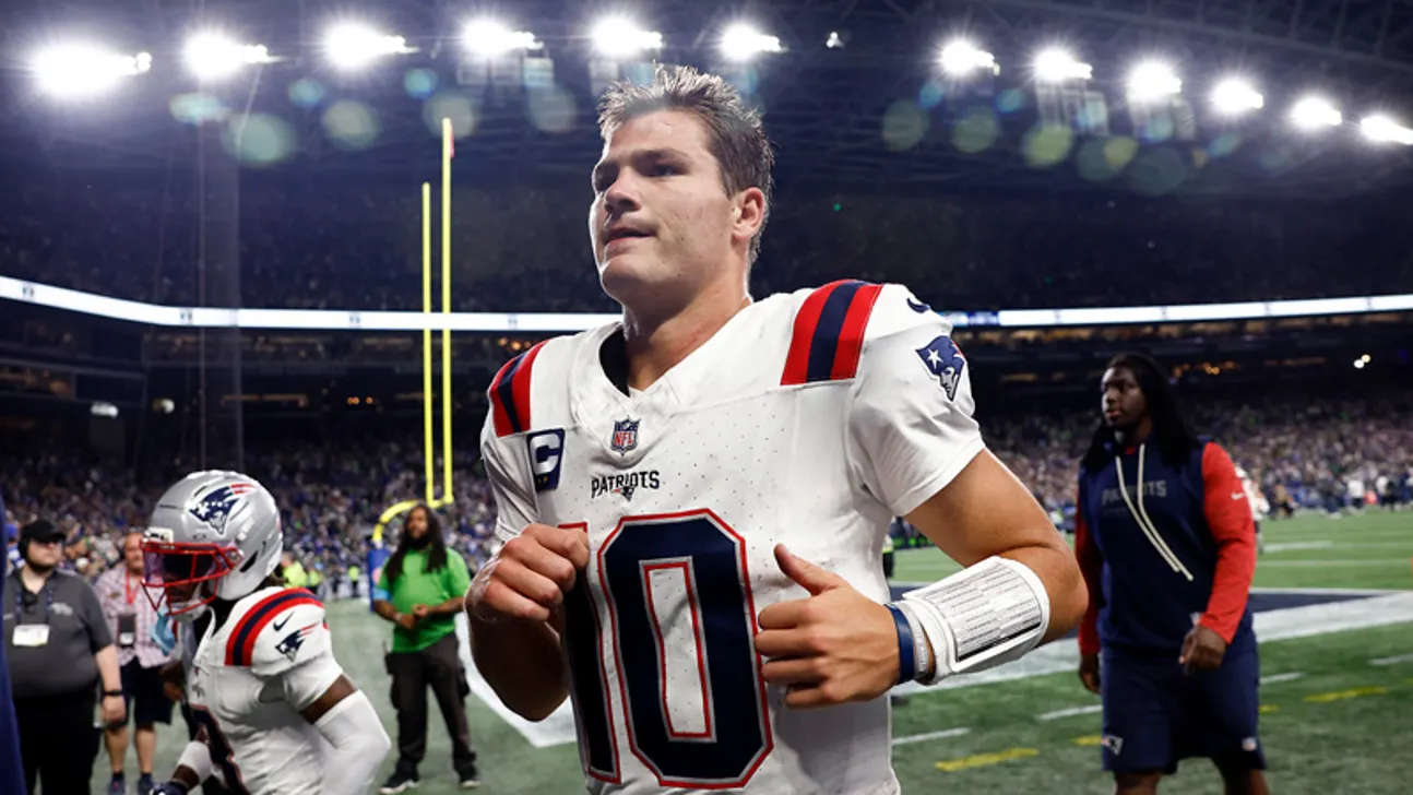 Patriots quarterback in white uniform jogging across a brightly lit football field