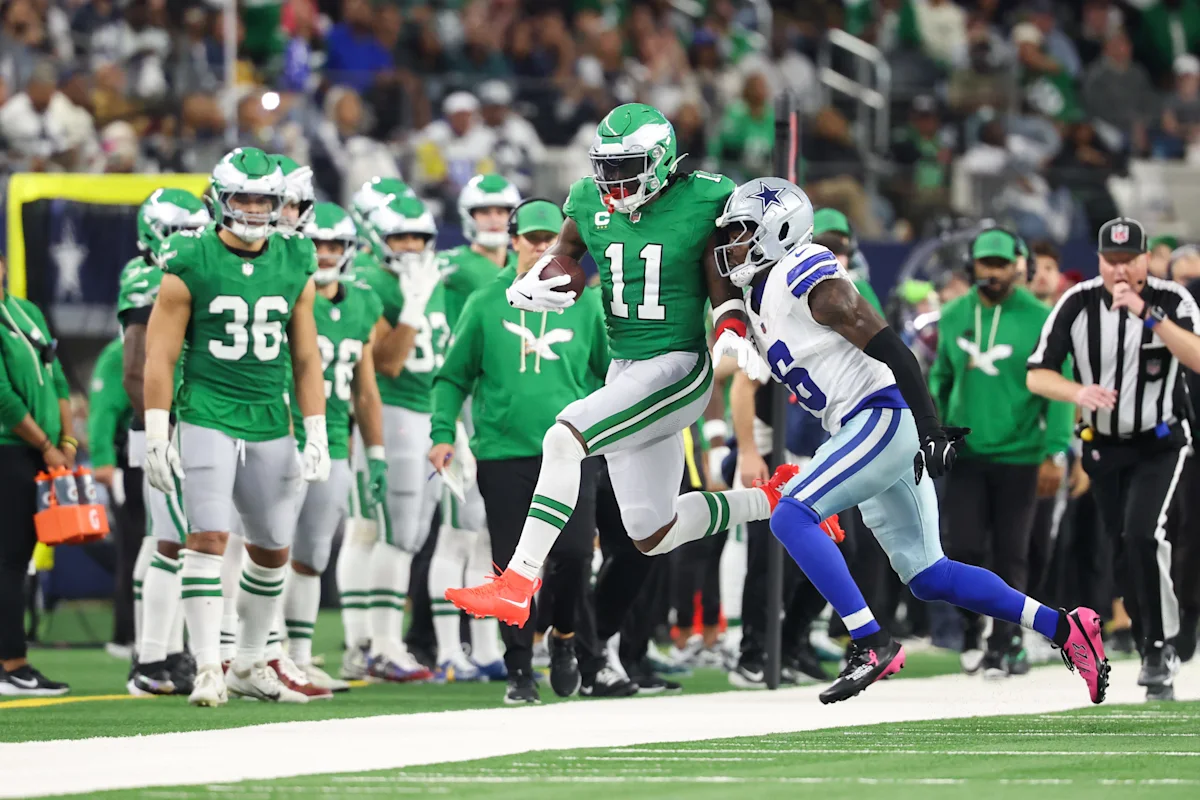 Football player in green jersey runs with the ball as a defender in white pursues.