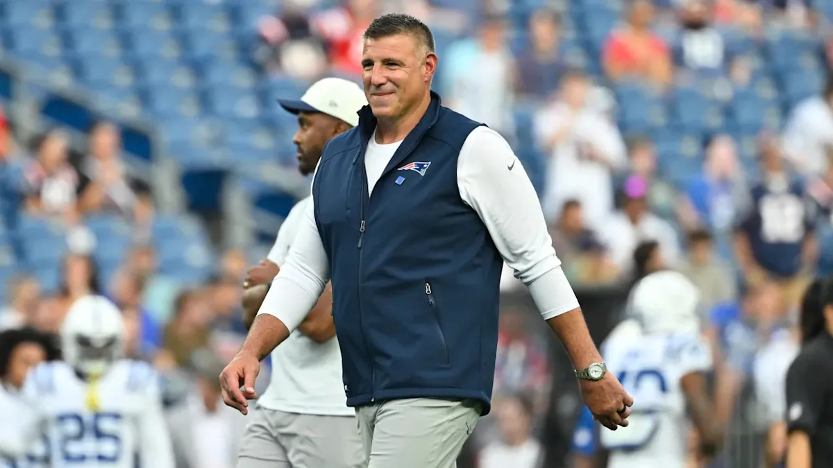 Football coach in Patriots vest walking across field during a game
