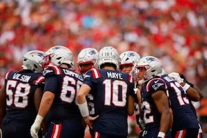 Football players in navy uniforms and helmets huddle together on the field.