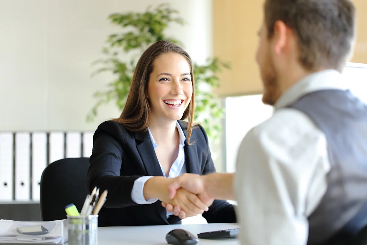 Smiling businesswoman shakes hands with a man across an office desk