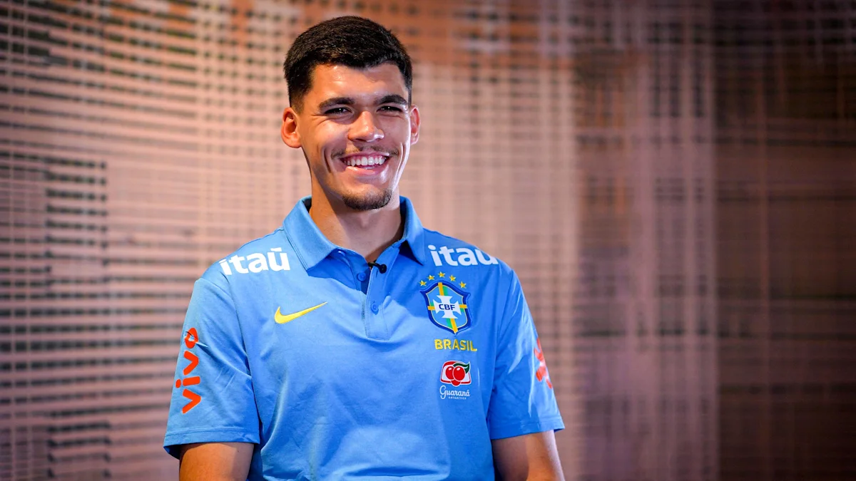Smiling man in a blue Brazil football polo stands before a patterned wall.