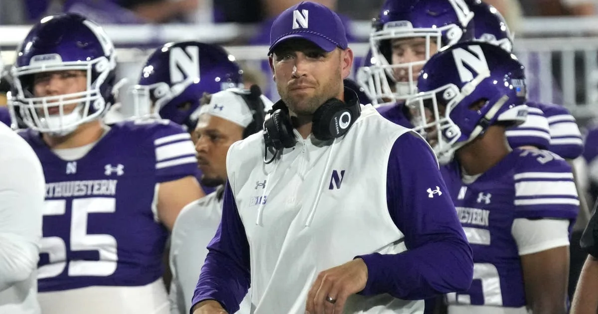 A Northwestern coach in a white vest stands among football players wearing purple helmets and uniforms.
