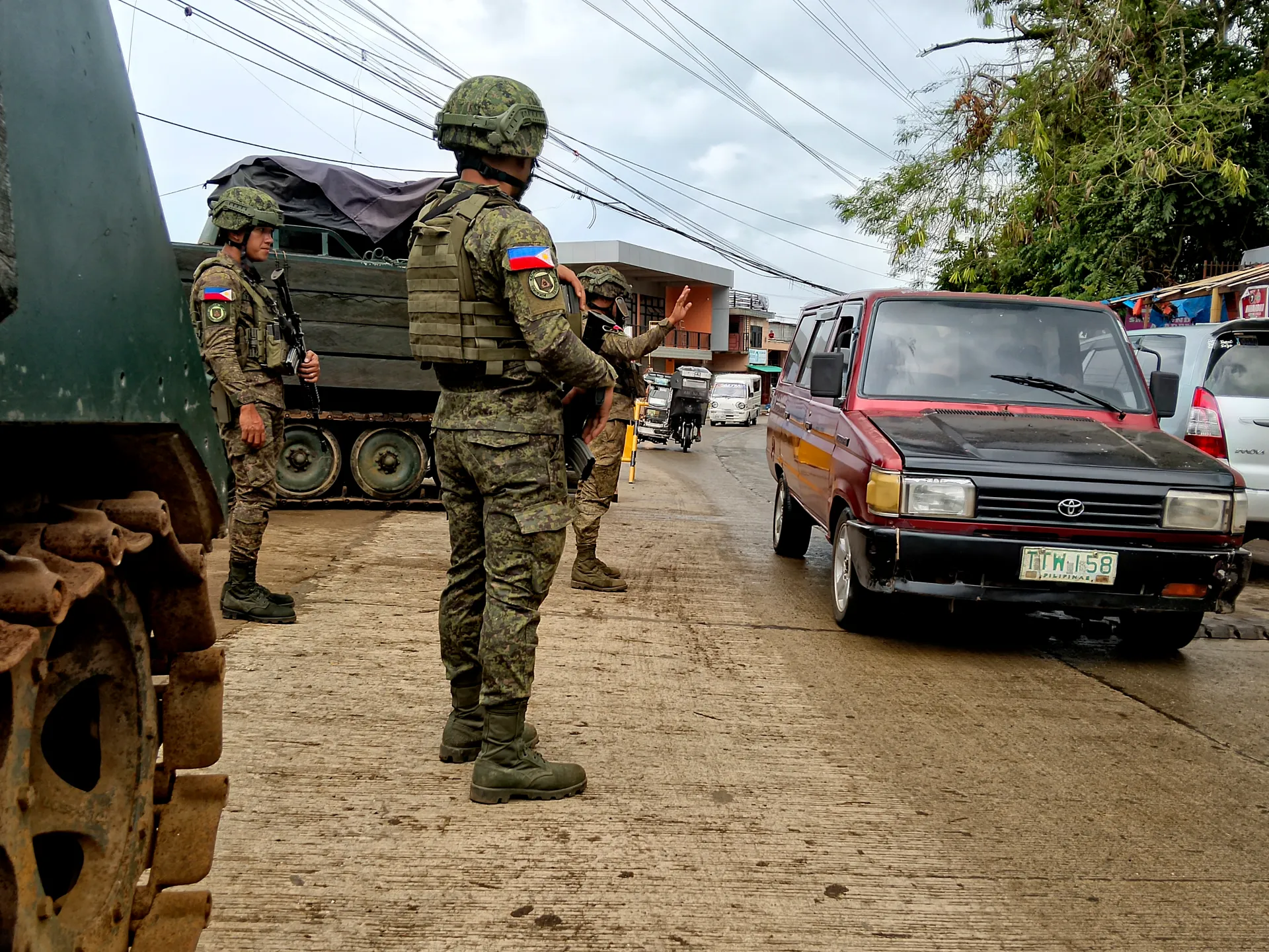Philippine soldiers stand beside an armored vehicle as a red van passes on a street