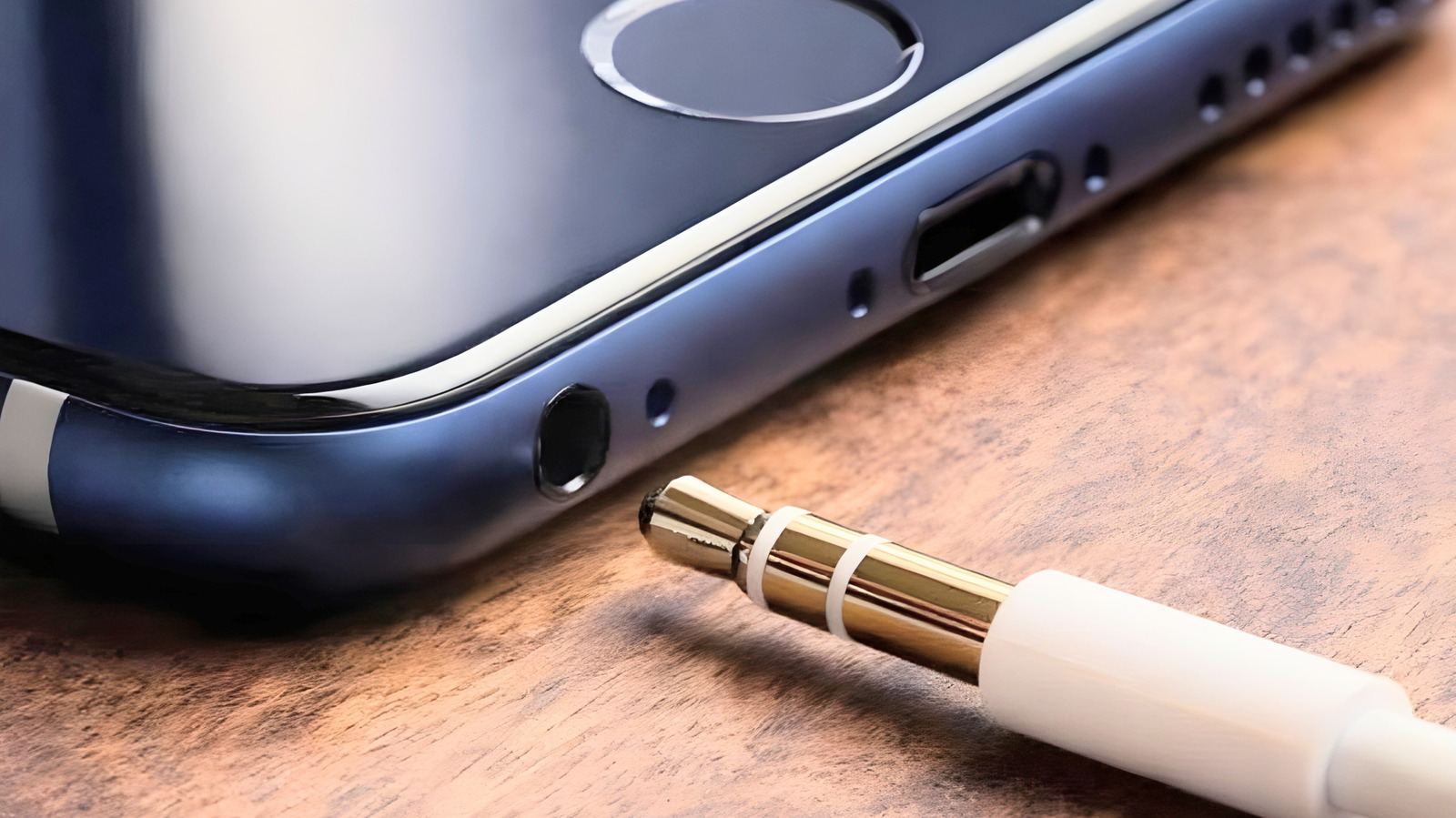 Close-up of a smartphone edge beside a white-and-gold audio cable on a wooden surface