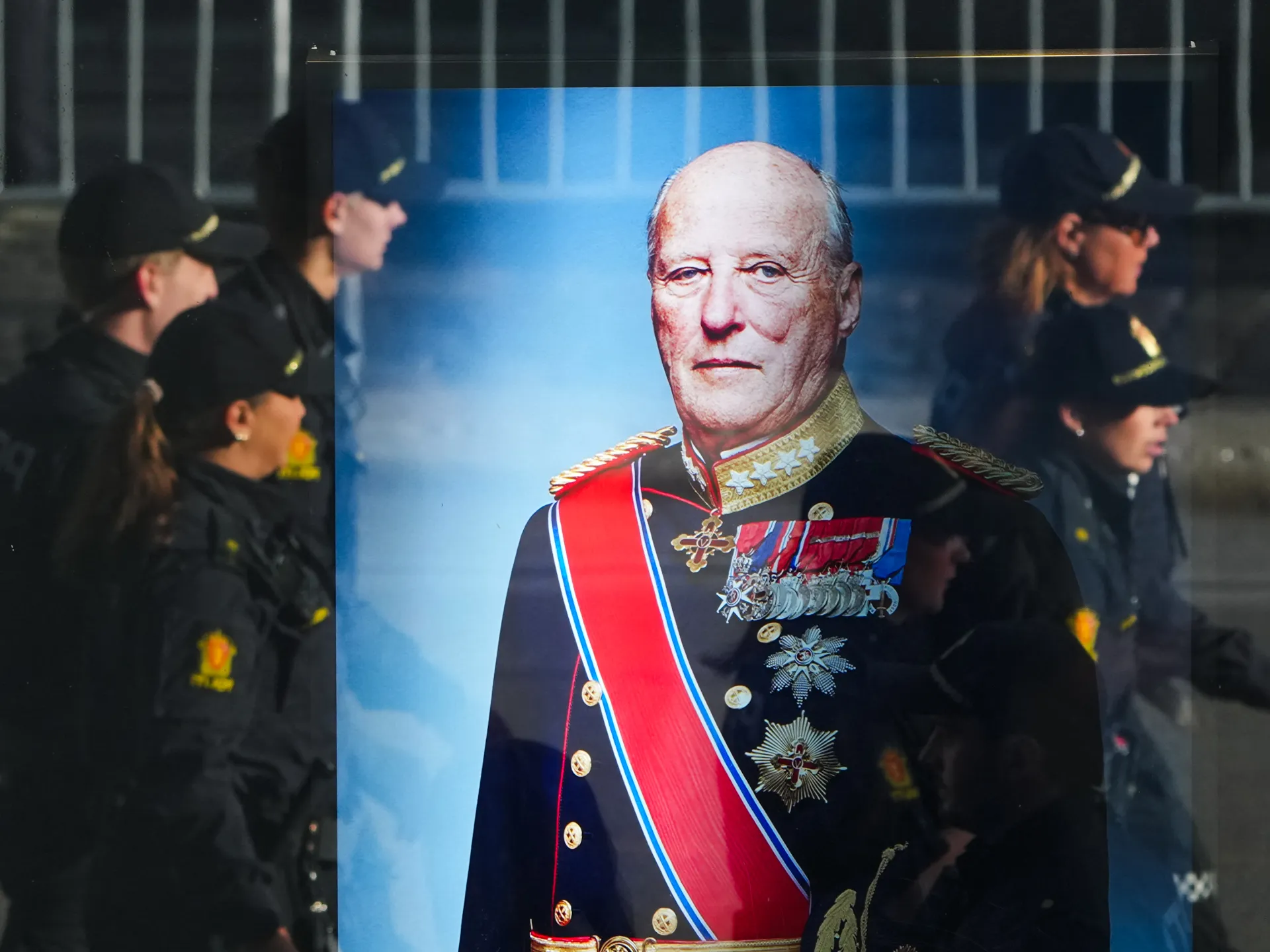 Large portrait of an elderly uniformed man displayed before people gathered in dark clothing