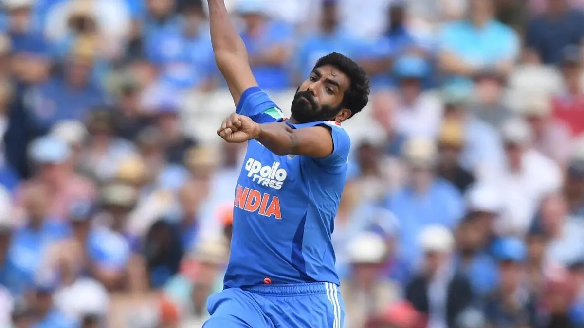 Indian cricketer in blue jersey delivering a bowling action before a blurred crowd