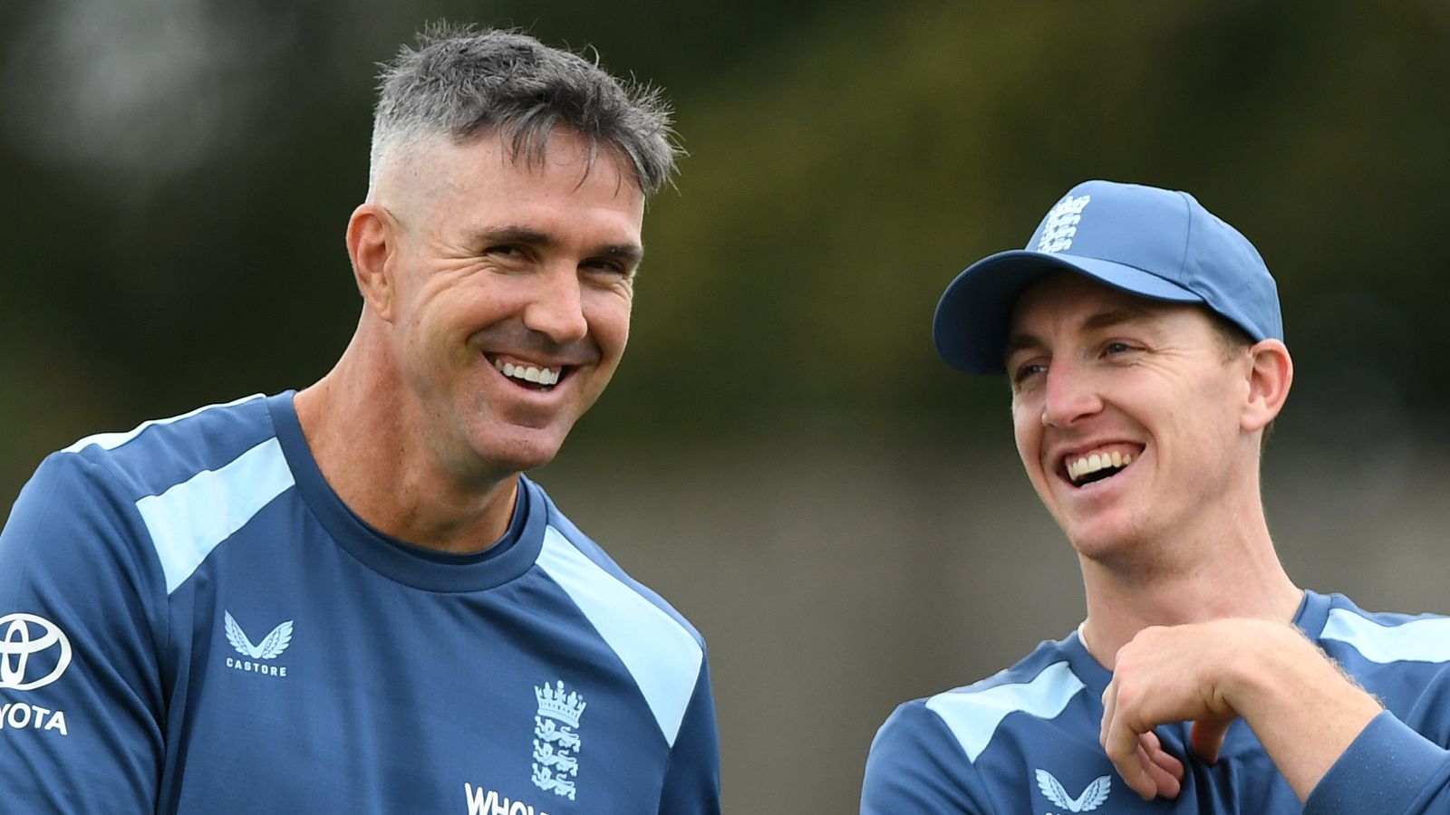 Two England cricketers in training shirts laugh together during a practice session.