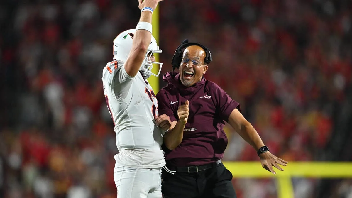A Virginia Tech coach celebrates beside a white-uniformed football player raising an arm during a game.